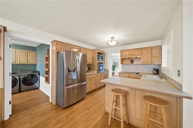 kitchen featuring light brown cabinetry, a breakfast bar area, washer and dryer, appliances with stainless steel finishes, and kitchen peninsula