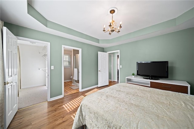 bedroom with hardwood / wood-style flooring, an inviting chandelier, and a tray ceiling