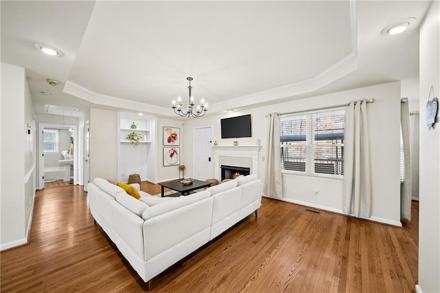 living room with hardwood / wood-style floors, built in features, a notable chandelier, a raised ceiling, and crown molding