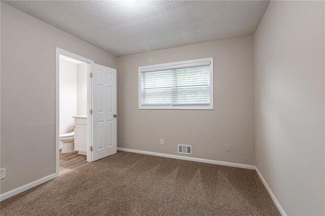 unfurnished bedroom featuring carpet, a textured ceiling, and ensuite bathroom