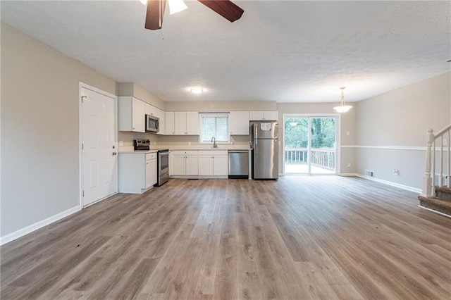 kitchen featuring appliances with stainless steel finishes, white cabinets, pendant lighting, light wood-type flooring, and ceiling fan