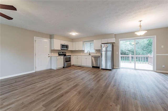 kitchen featuring appliances with stainless steel finishes, white cabinets, pendant lighting, wood-type flooring, and ceiling fan