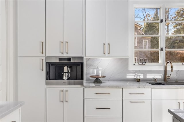 bar with tasteful backsplash, white cabinetry, sink, and light stone counters