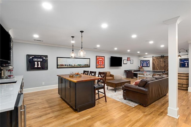 bar featuring dark brown cabinetry, a barn door, crown molding, pendant lighting, and light wood-type flooring