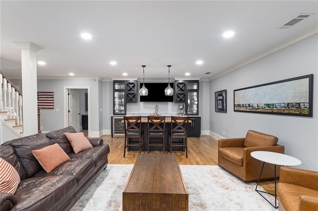 living room with decorative columns, crown molding, indoor bar, light hardwood / wood-style floors, and wine cooler