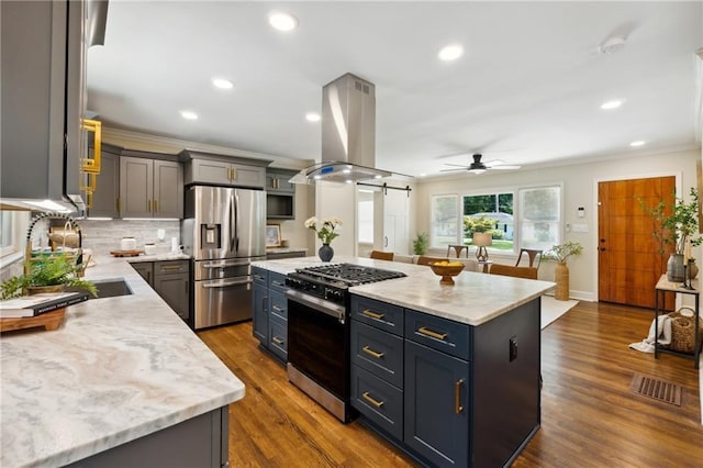 kitchen with island exhaust hood, appliances with stainless steel finishes, ceiling fan, a barn door, and a kitchen island