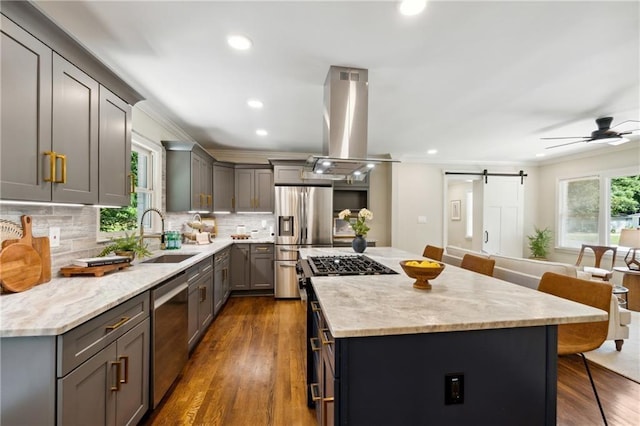 kitchen with sink, stainless steel appliances, a kitchen breakfast bar, a barn door, and island exhaust hood