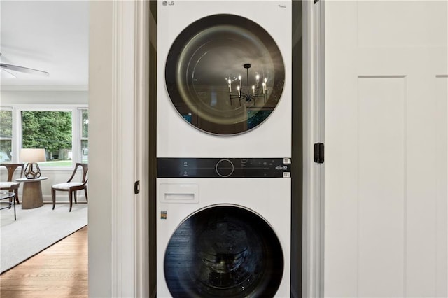 washroom featuring wood-type flooring, ceiling fan with notable chandelier, stacked washing maching and dryer, and ornamental molding