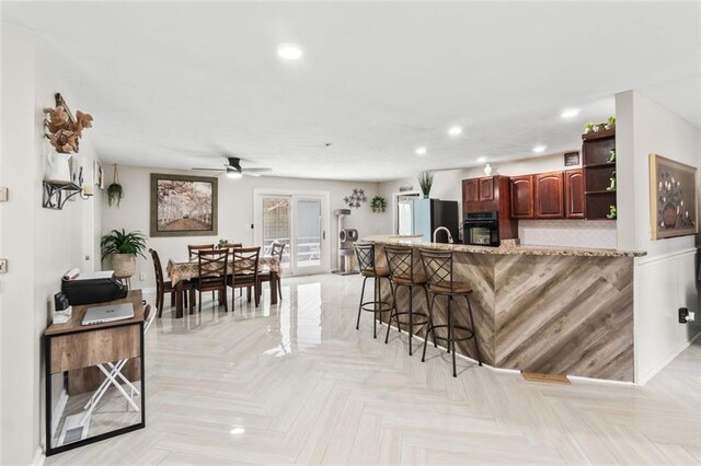 kitchen with oven, freestanding refrigerator, ceiling fan, open shelves, and a breakfast bar area
