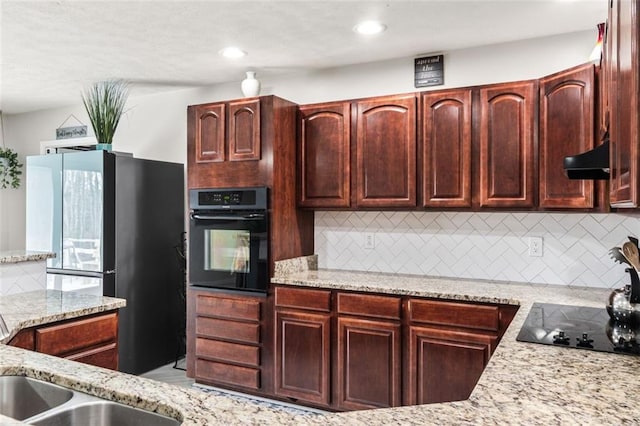 kitchen featuring a sink, black appliances, backsplash, range hood, and light stone countertops