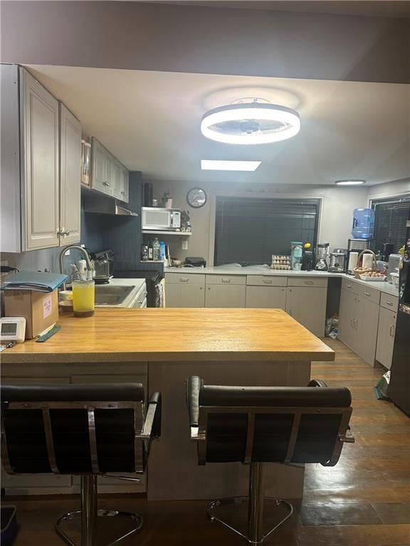 kitchen featuring light countertops, a sink, a breakfast bar, a peninsula, and white microwave