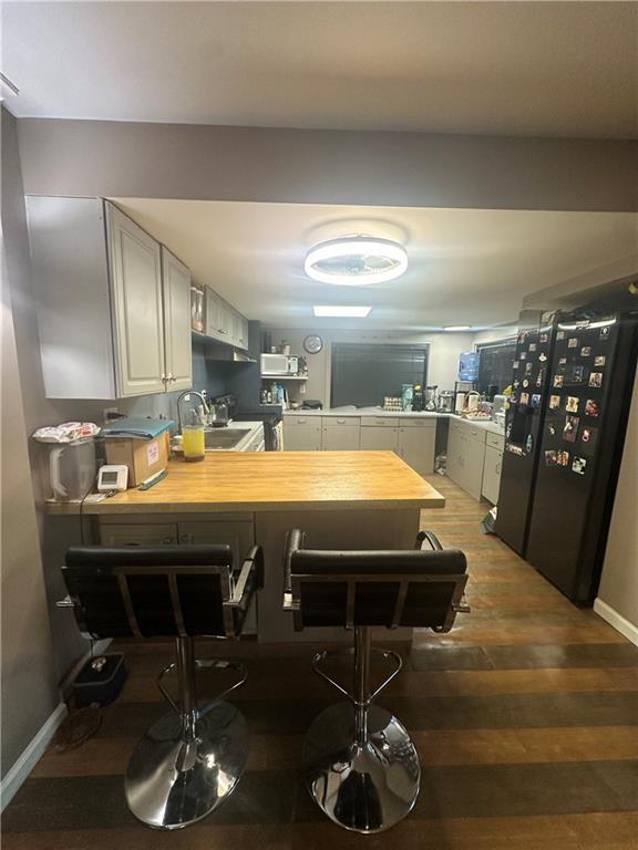 kitchen with black fridge with ice dispenser, light countertops, a peninsula, wood finished floors, and a sink