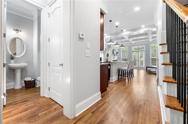 corridor with ornamental molding, coffered ceiling, recessed lighting, light wood finished floors, and baseboards