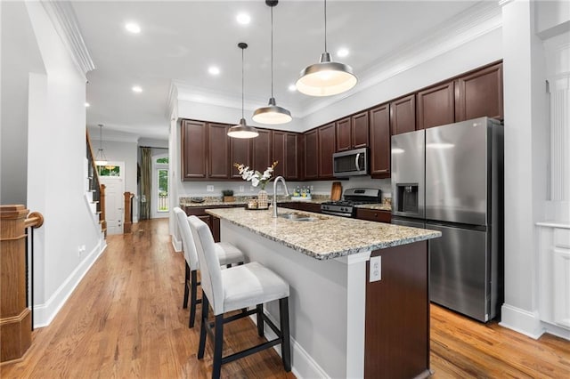 kitchen featuring appliances with stainless steel finishes, ornamental molding, a sink, dark brown cabinetry, and an island with sink