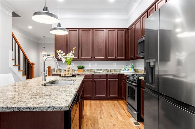 kitchen featuring appliances with stainless steel finishes, a sink, light wood-type flooring, pendant lighting, and ornamental molding