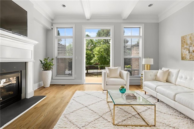living room featuring a glass covered fireplace, light wood-type flooring, healthy amount of natural light, beam ceiling, and crown molding