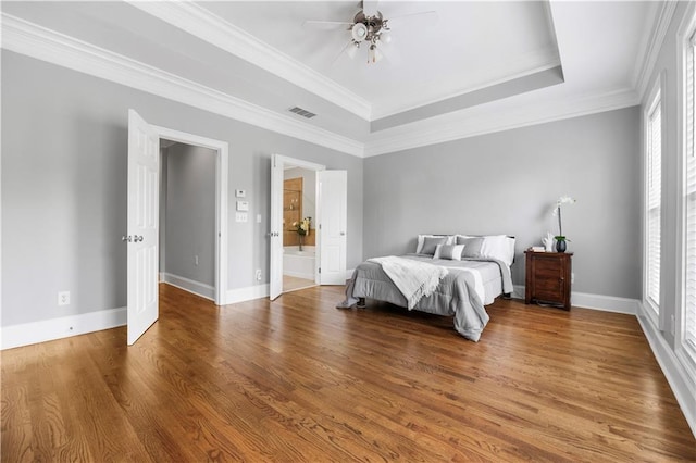 bedroom featuring multiple windows, wood finished floors, a raised ceiling, ornamental molding, and baseboards