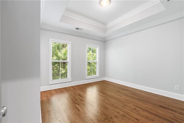 spare room with a tray ceiling, dark wood-type flooring, baseboards, and ornamental molding