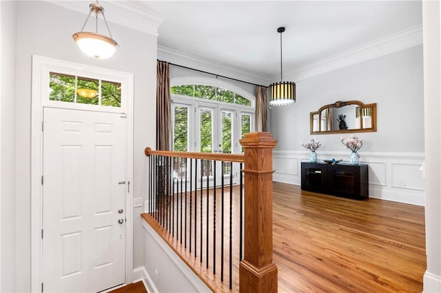 foyer entrance featuring wood finished floors, ornamental molding, and a wainscoted wall