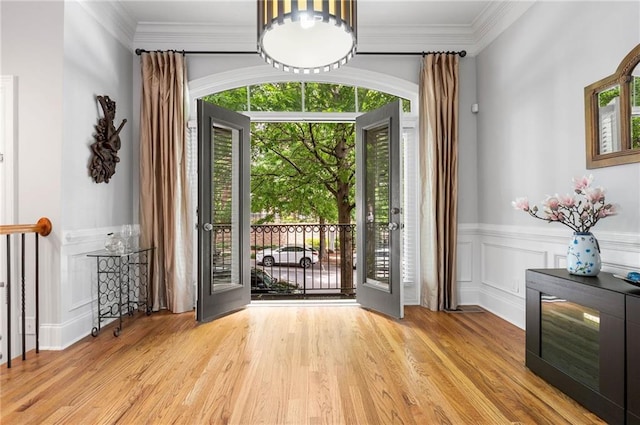 foyer entrance featuring wainscoting, light wood finished floors, crown molding, and a decorative wall