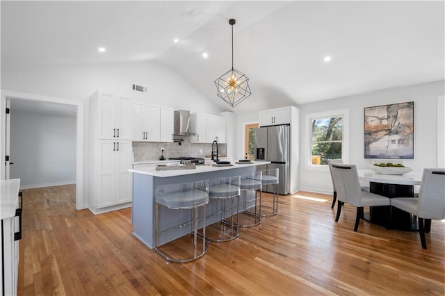 kitchen with light wood finished floors, white cabinets, light countertops, wall chimney range hood, and stainless steel refrigerator with ice dispenser