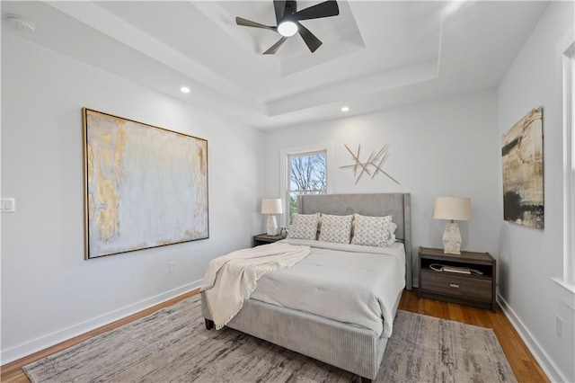 bedroom featuring baseboards, ceiling fan, wood finished floors, a tray ceiling, and recessed lighting