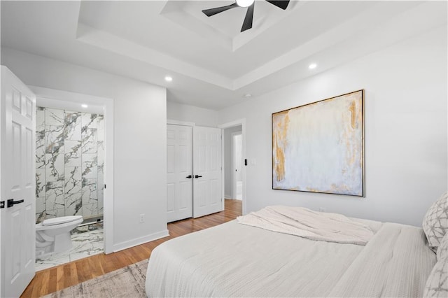 bedroom featuring a tray ceiling, recessed lighting, a ceiling fan, wood finished floors, and baseboards