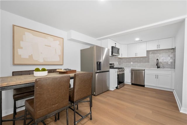 kitchen featuring stainless steel appliances, light countertops, backsplash, light wood-style flooring, and white cabinetry