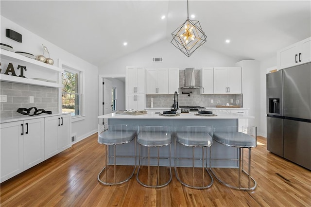 kitchen featuring wall chimney exhaust hood, visible vents, stainless steel refrigerator with ice dispenser, and light countertops