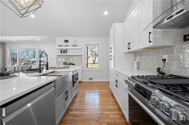 kitchen featuring light wood-style flooring, stainless steel appliances, exhaust hood, visible vents, and a wealth of natural light