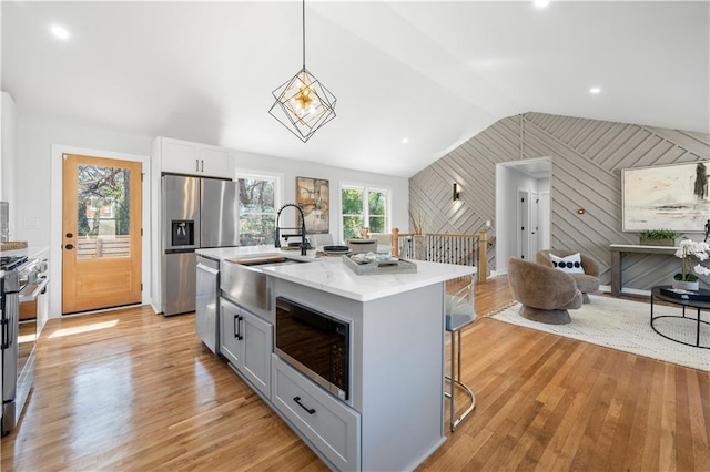 kitchen with stainless steel appliances, a kitchen breakfast bar, vaulted ceiling, gray cabinets, and light wood finished floors