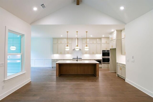 kitchen with stainless steel double oven, dark wood-type flooring, sink, pendant lighting, and a center island with sink