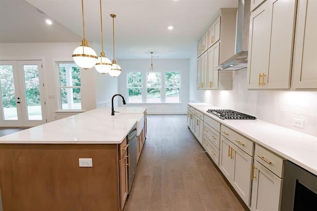 kitchen with hardwood / wood-style floors, wall chimney exhaust hood, hanging light fixtures, and a large island with sink