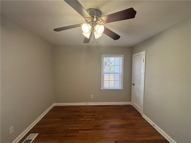 spare room with a ceiling fan, dark wood finished floors, visible vents, and baseboards