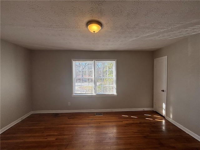 empty room featuring a textured ceiling, dark wood-style flooring, visible vents, and baseboards