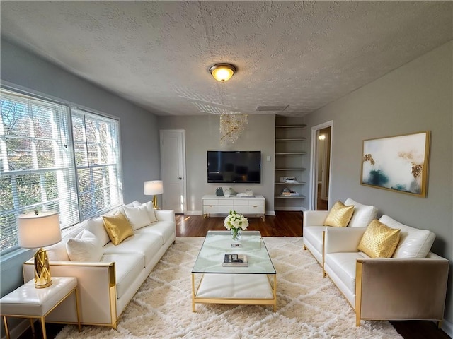 living area featuring built in features, baseboards, a textured ceiling, and light wood finished floors