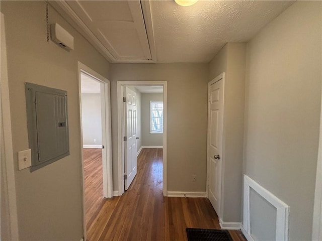 corridor featuring dark wood-style floors, visible vents, attic access, electric panel, and baseboards