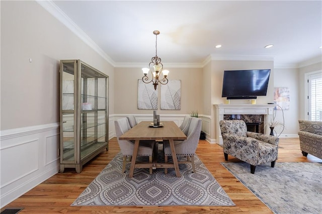 dining area featuring crown molding, a chandelier, a premium fireplace, light wood-style flooring, and wainscoting