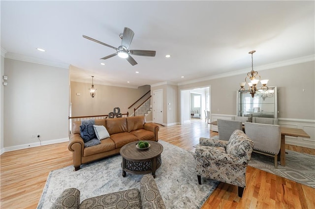 living area featuring stairway, wood finished floors, crown molding, and ceiling fan with notable chandelier