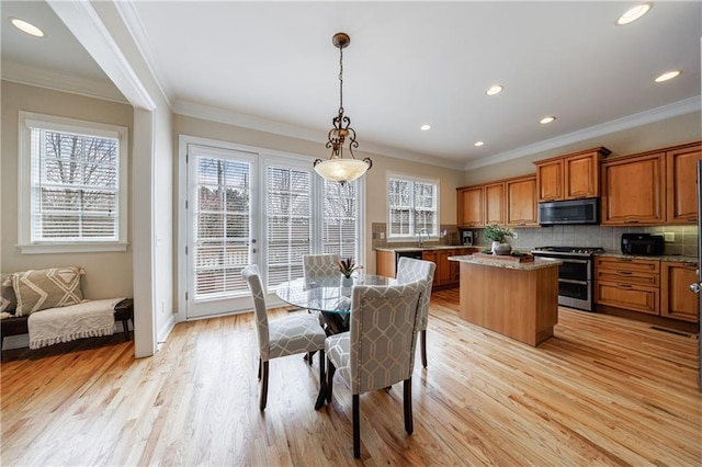 dining space featuring light wood-type flooring, a healthy amount of sunlight, and crown molding
