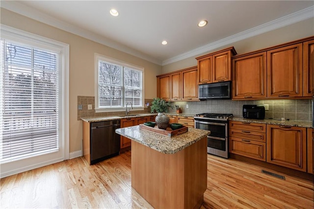 kitchen featuring crown molding, light wood-style floors, brown cabinetry, stainless steel appliances, and a sink