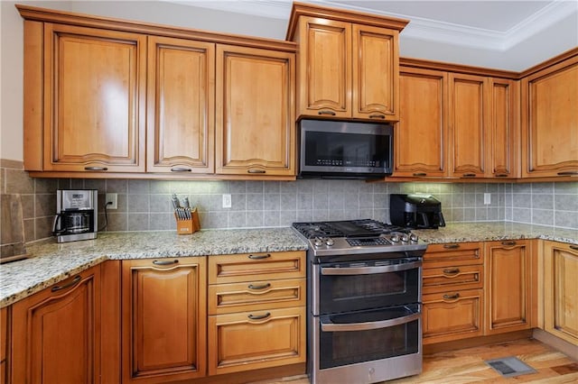 kitchen featuring ornamental molding, light stone counters, tasteful backsplash, stainless steel appliances, and brown cabinetry