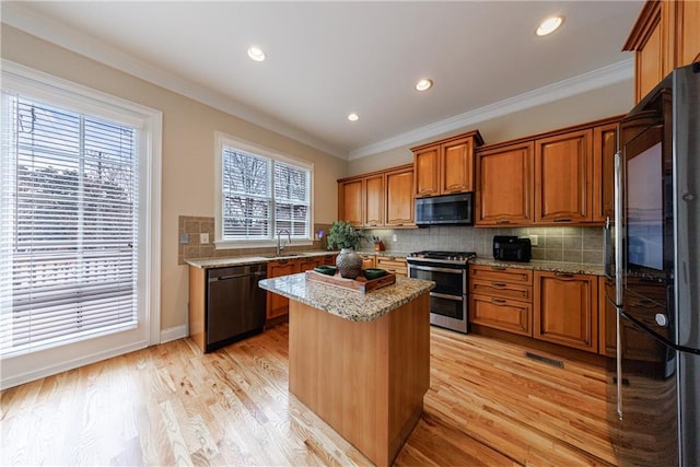 kitchen featuring black appliances, ornamental molding, brown cabinetry, and a sink