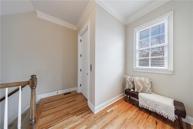 corridor featuring visible vents, baseboards, light wood-style flooring, and ornamental molding
