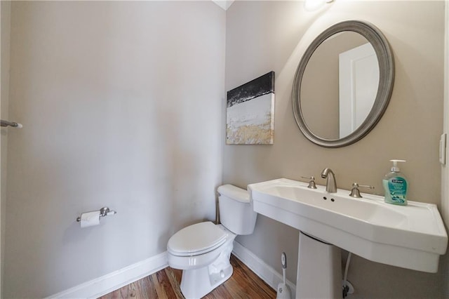 half bath with a sink, baseboards, toilet, and wood finished floors