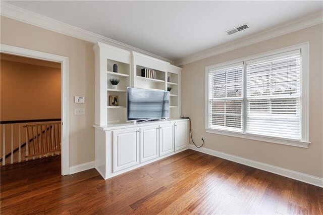 unfurnished living room featuring baseboards, wood finished floors, visible vents, and ornamental molding