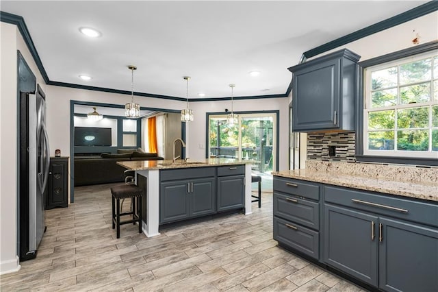 kitchen with light hardwood / wood-style floors, a center island with sink, decorative light fixtures, light stone countertops, and stainless steel fridge