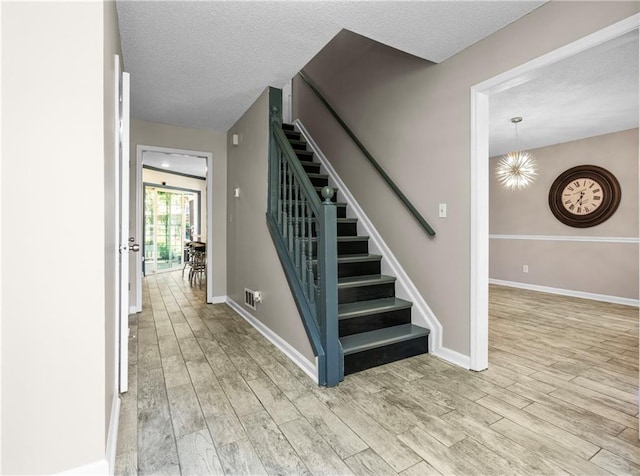 staircase featuring an inviting chandelier, hardwood / wood-style floors, and a textured ceiling