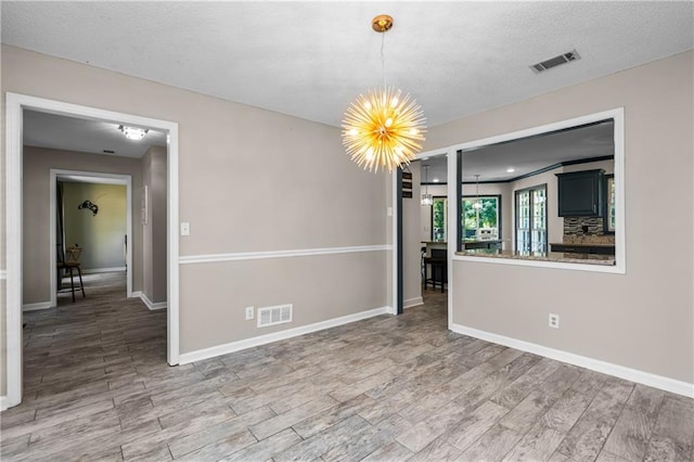 unfurnished room featuring an inviting chandelier, a textured ceiling, and hardwood / wood-style floors