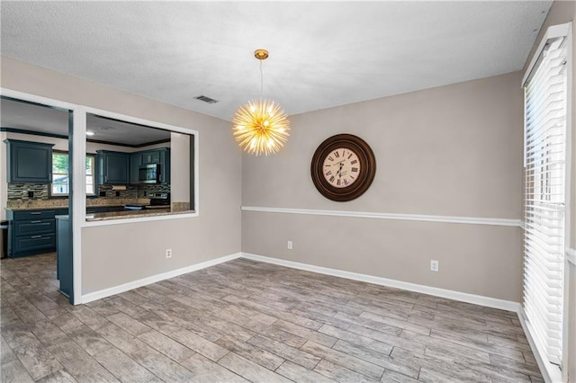 unfurnished dining area featuring an inviting chandelier, hardwood / wood-style floors, a textured ceiling, and a healthy amount of sunlight